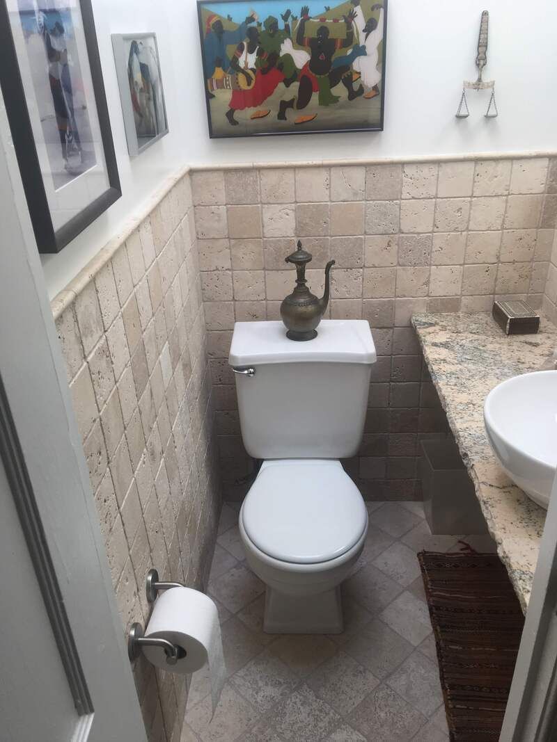Small bathroom with a toilet, sink, and artwork on the walls. Beige tiled walls and floor.
