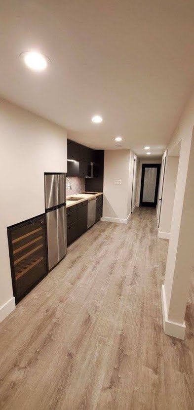 A modern kitchen with dark cabinets, stainless steel appliances, and light wood flooring.