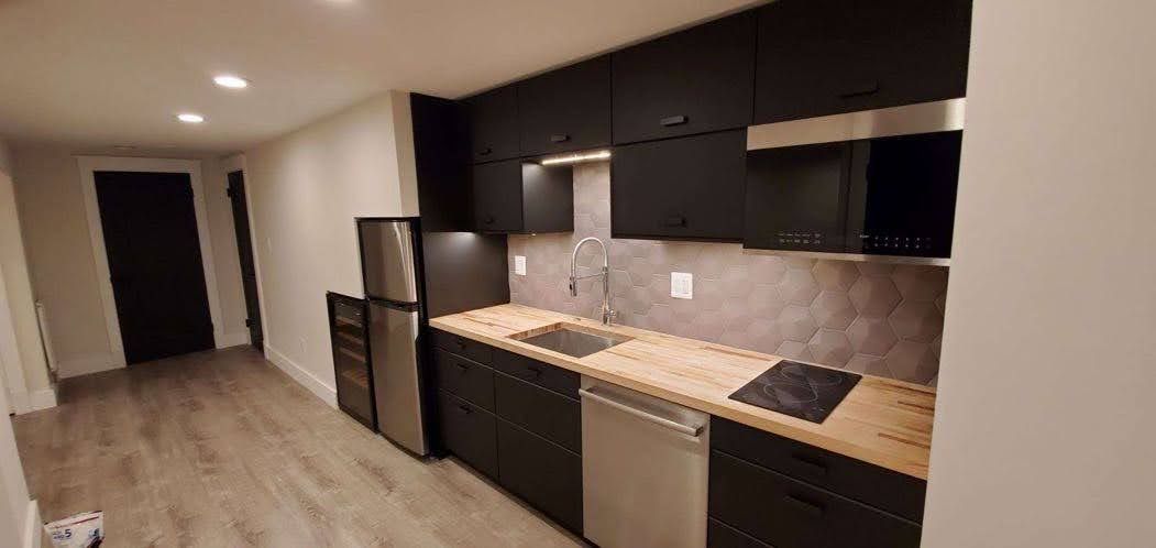 Modern kitchen with black cabinets, stainless steel appliances, and wood countertops.