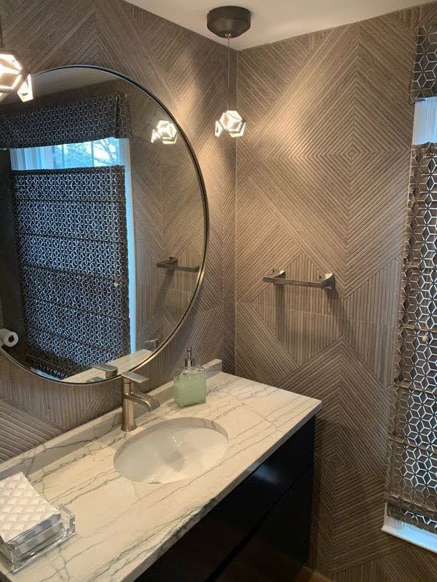 Powder room with a marble countertop vanity, round mirror, and patterned wallpaper.