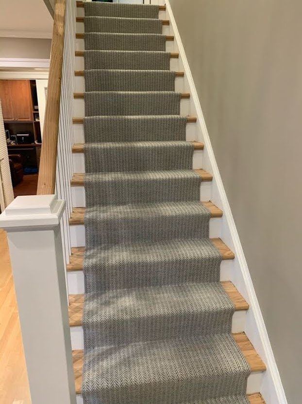 Staircase with gray carpet runner, wood steps, white banister, and gray wall.