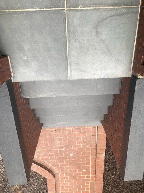 Staircase with gray steps, brick walls, and top landing, descending into a brick-paved area.