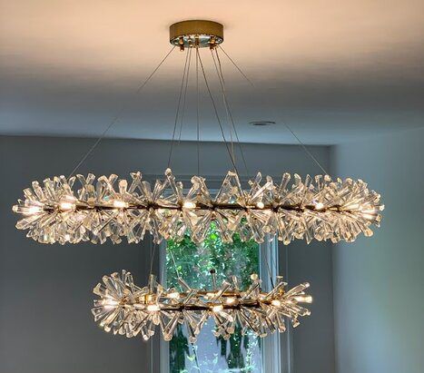 Two-tiered crystal chandelier hanging from the ceiling above a window, with sparkling lights and an ornate design.