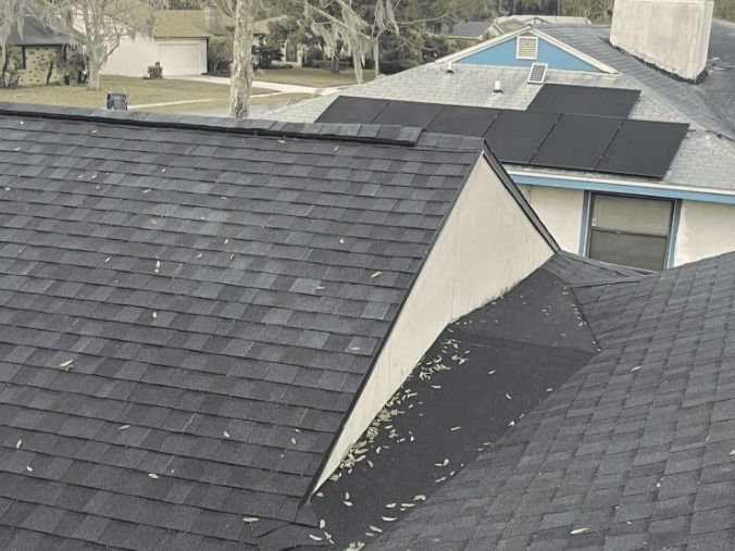 Overhead view of multiple houses with dark shingled roofs, some with solar panels, under a cloudy sky.