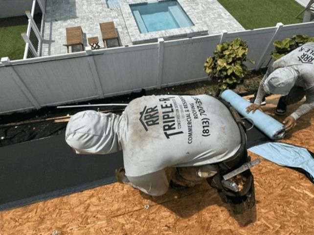 Two roofers installing roofing material near a white fence and pool.