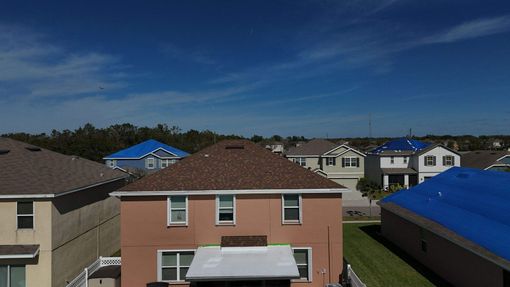 Two roofers installing roofing material near a white fence and pool.