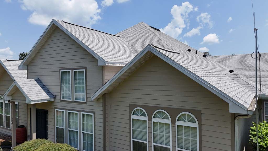 Tan house with gray roof against a blue sky, multiple windows, and a radio antenna.