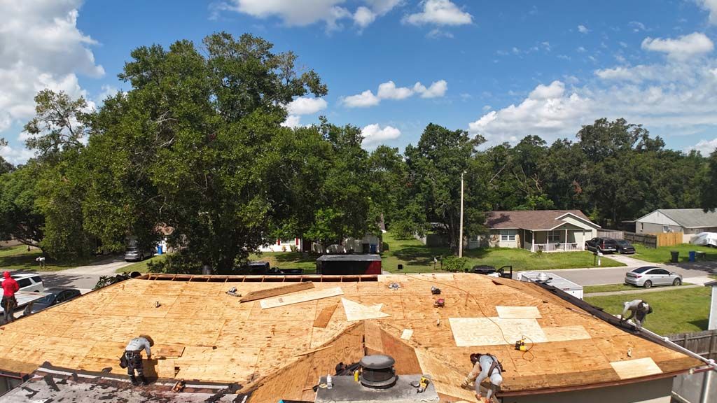Roofers working on a new roof, trees and houses in the background, blue sky with clouds.