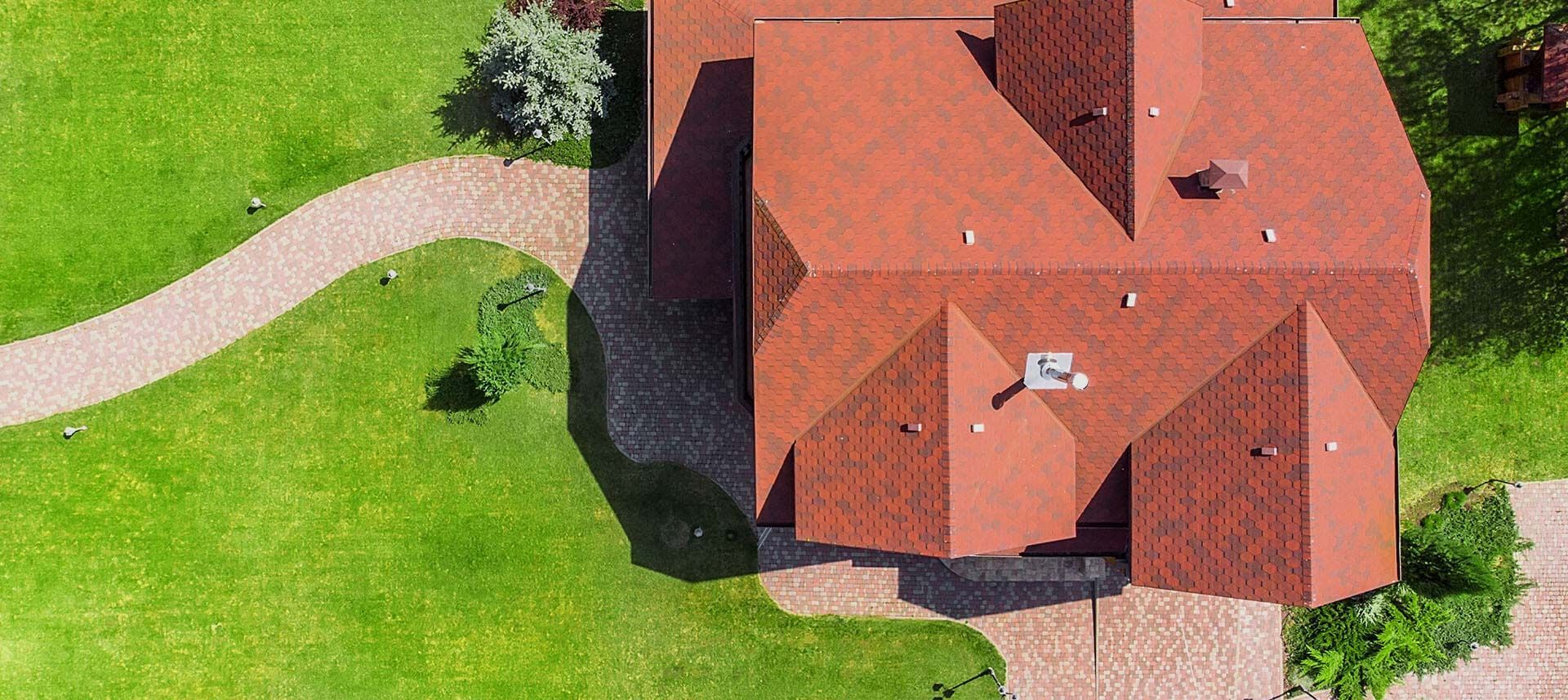 Overhead view of a house with a red roof and a stone path surrounded by green grass.