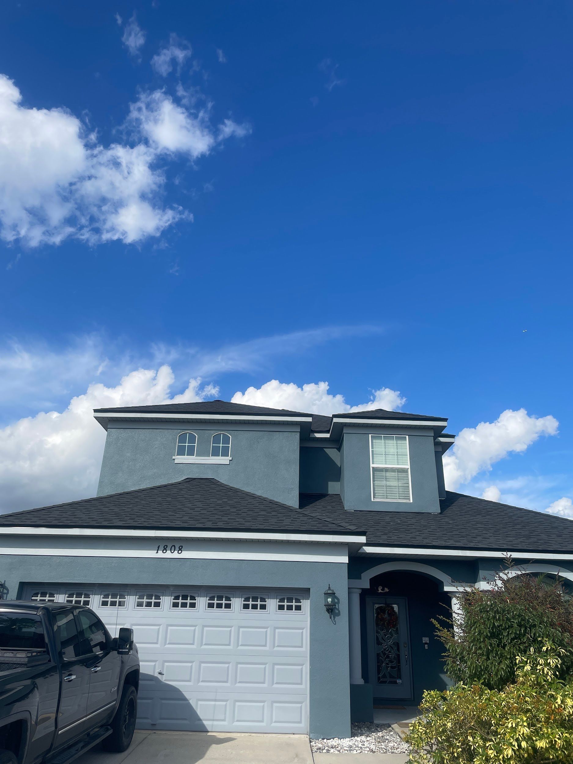 Blue house with gray roof and garage against a bright blue sky with scattered clouds.