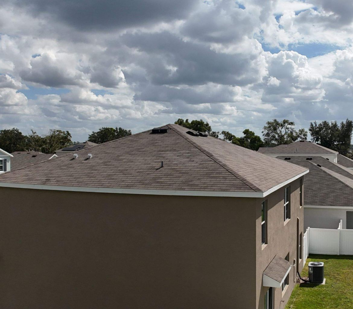 Brown house with a tan roof under a cloudy sky.
