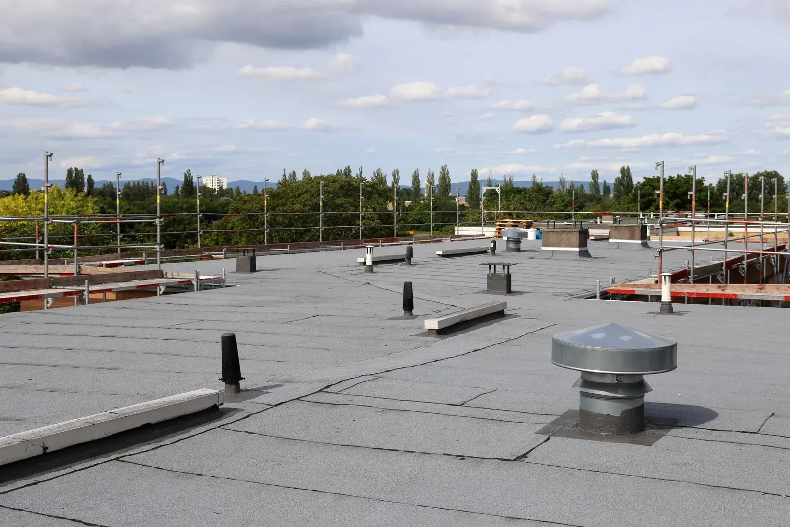 Flat commercial rooftop with vents, pipes, and safety railings under a cloudy sky.