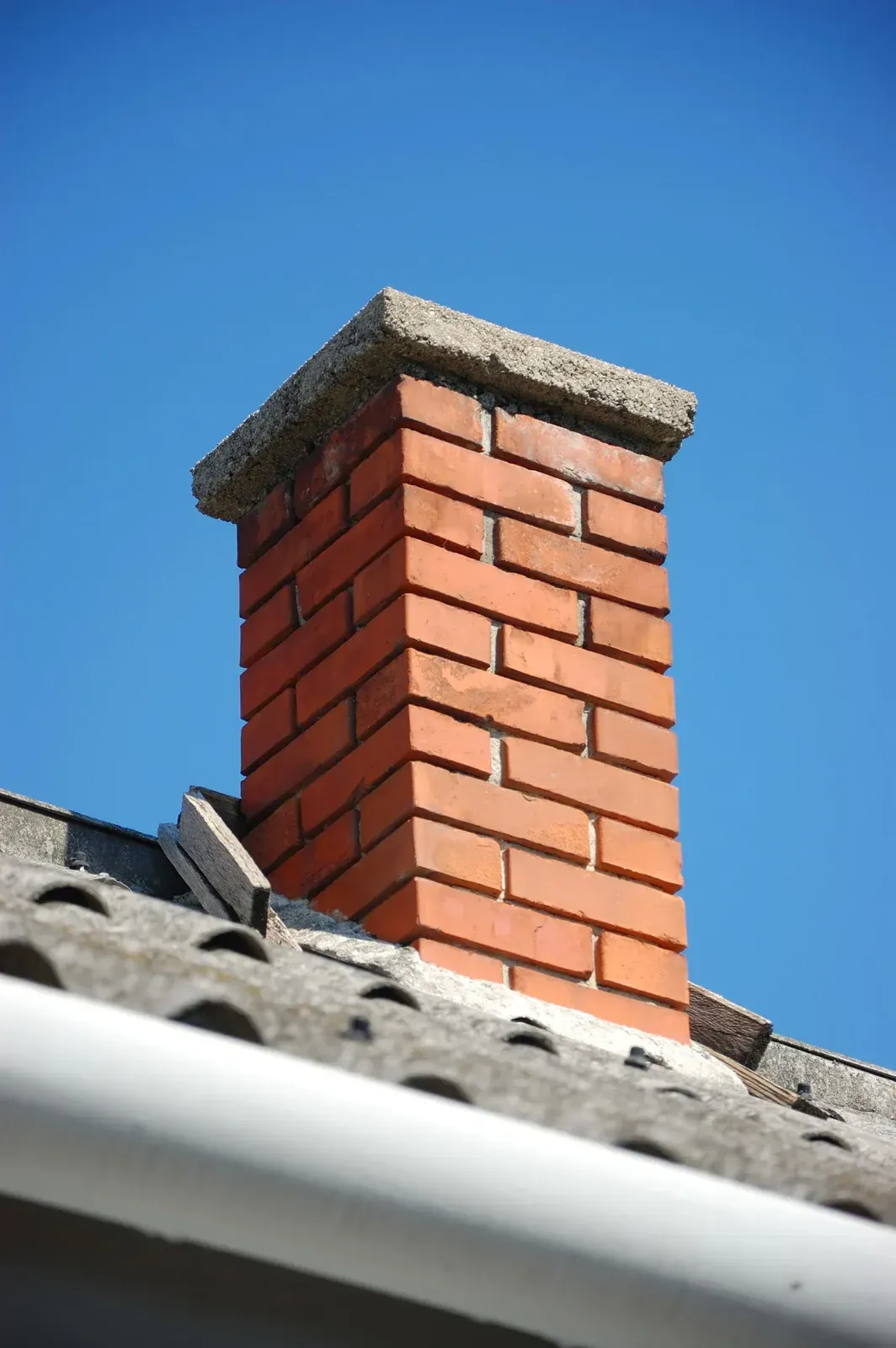 Brick chimney on a gray roof against a bright blue sky.
