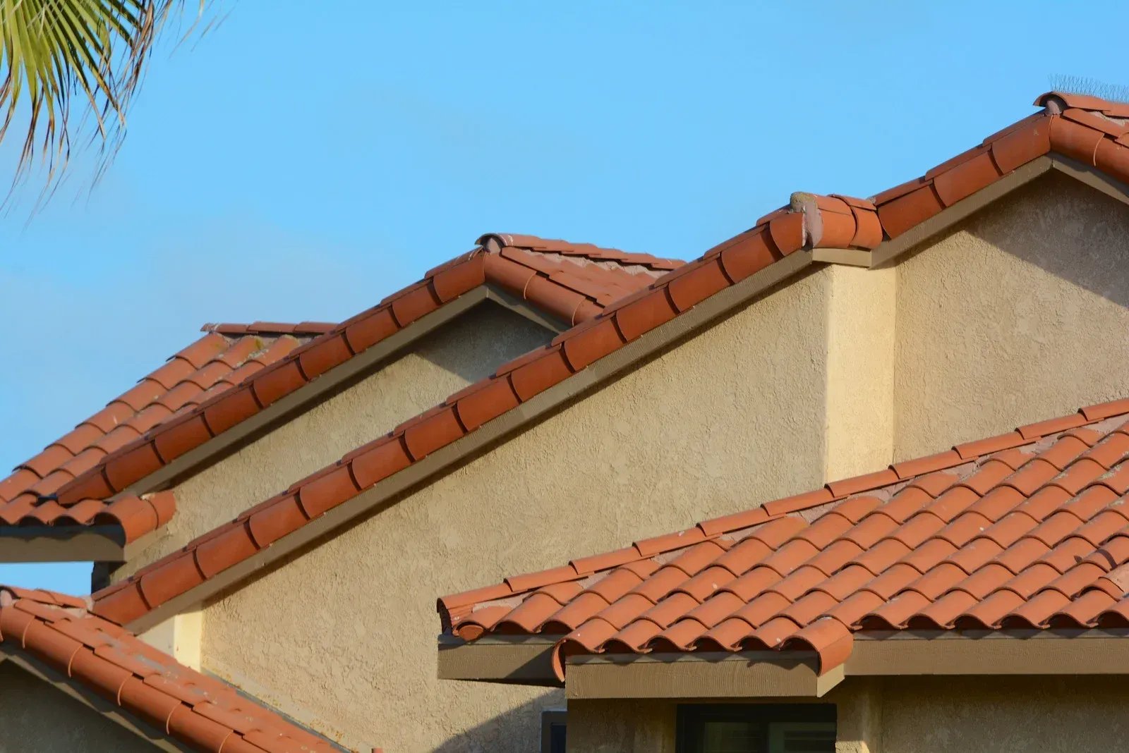 Tan stucco building with red tile roof against a blue sky.
