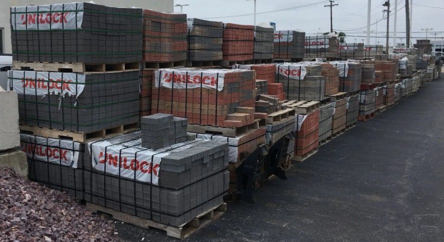 multiple stacks of landscaping pavers and bricks on wooden pallets in an outdoor supply yard.