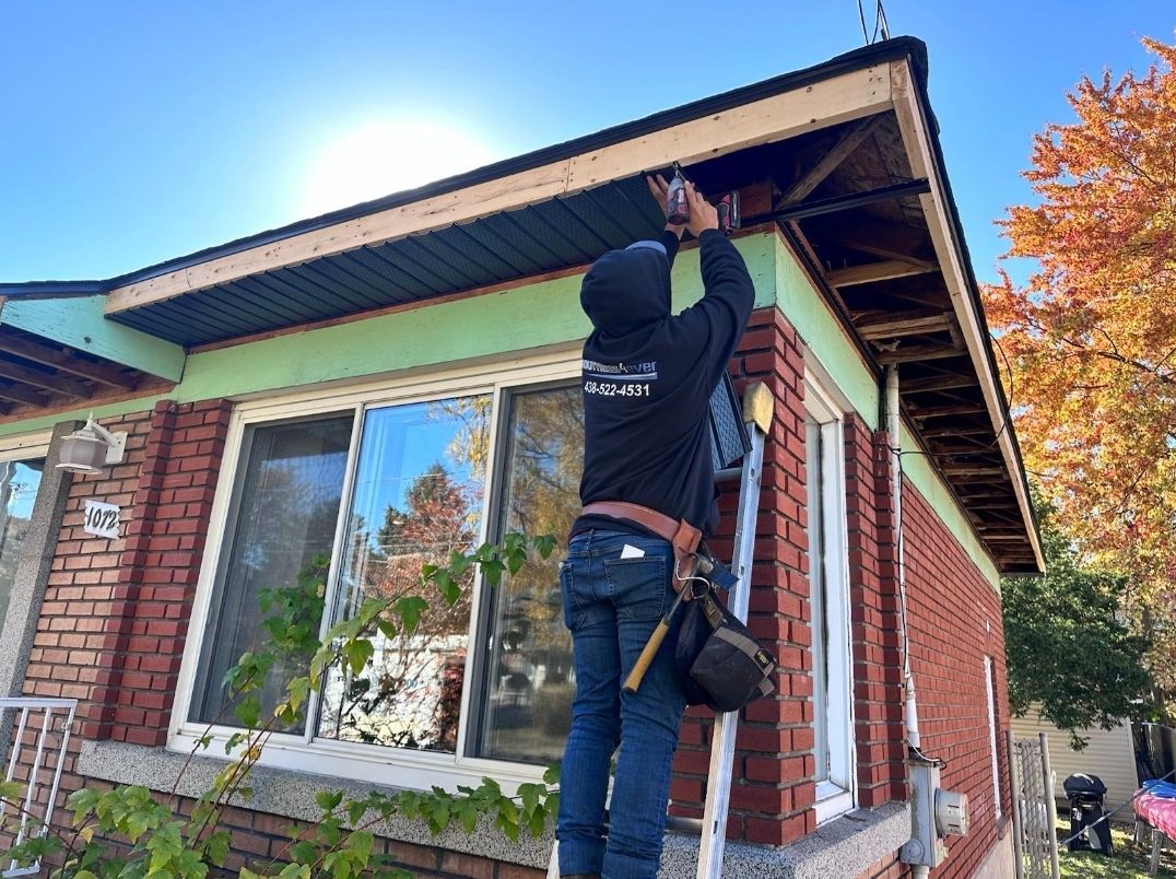 A man is standing on a ladder working on the roof of a house.