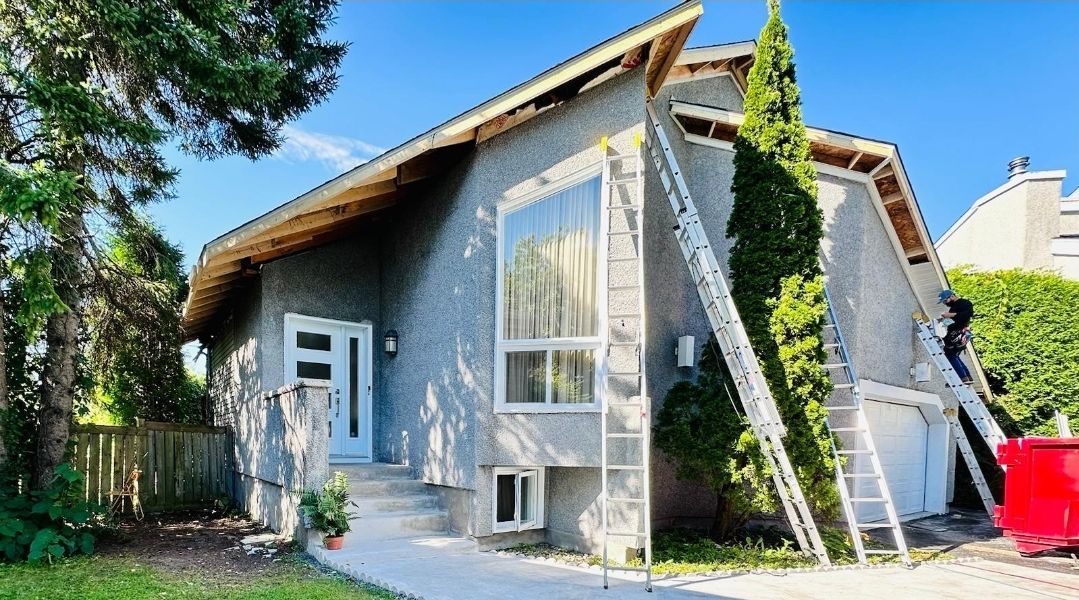 A man is painting the side of a house with a ladder.