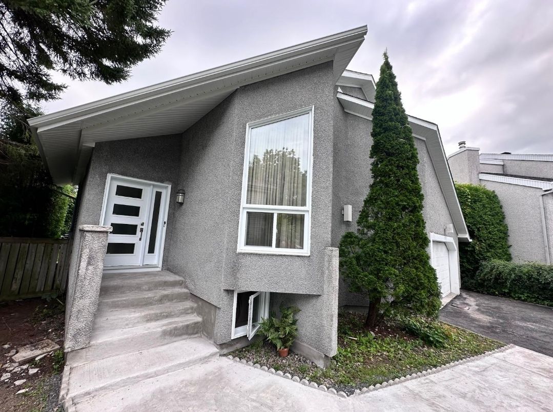A gray house with a white door and stairs and a tree in front of it.