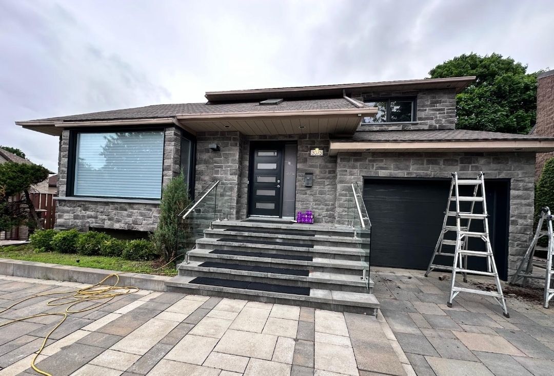 A large brick house with a black garage door is being painted.