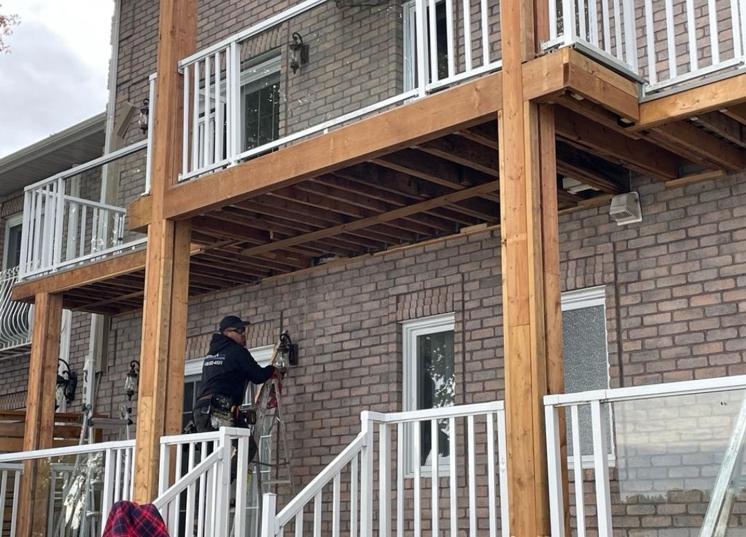 A man is standing on a balcony of a brick house.
