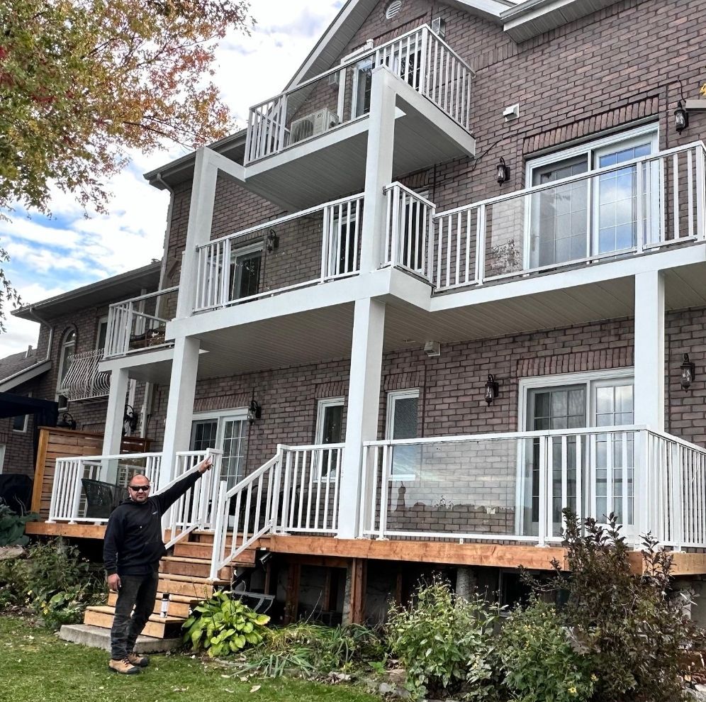 A man is standing in front of a large brick house with balconies.