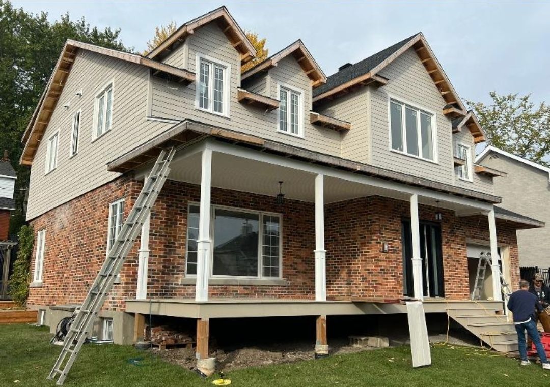 A large brick house with a porch and a ladder in front of it.