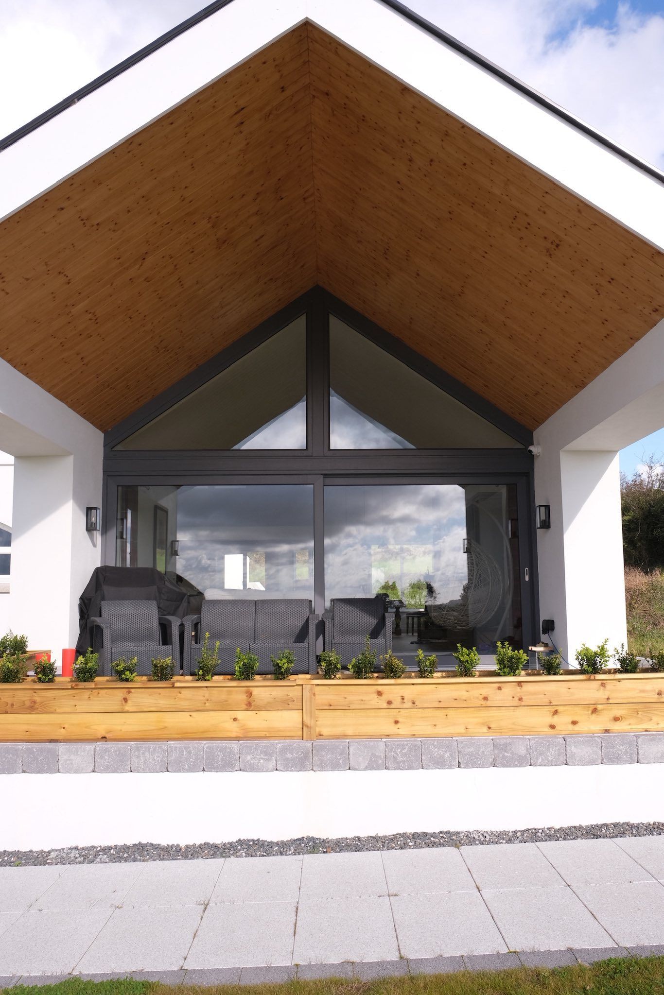 Modern house exterior with wooden porch and large glass doors.