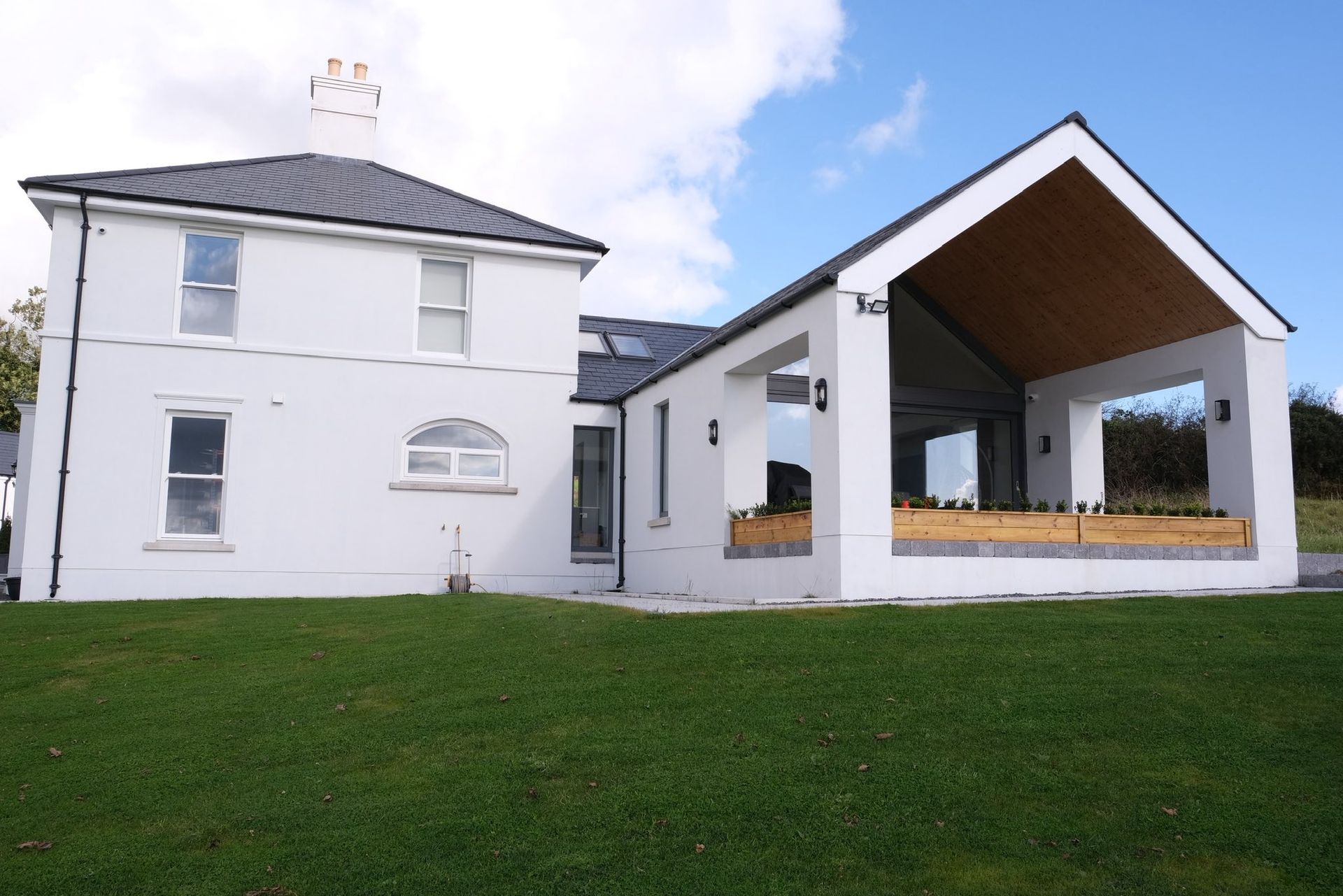 White house with a modern extension; green lawn and blue sky.