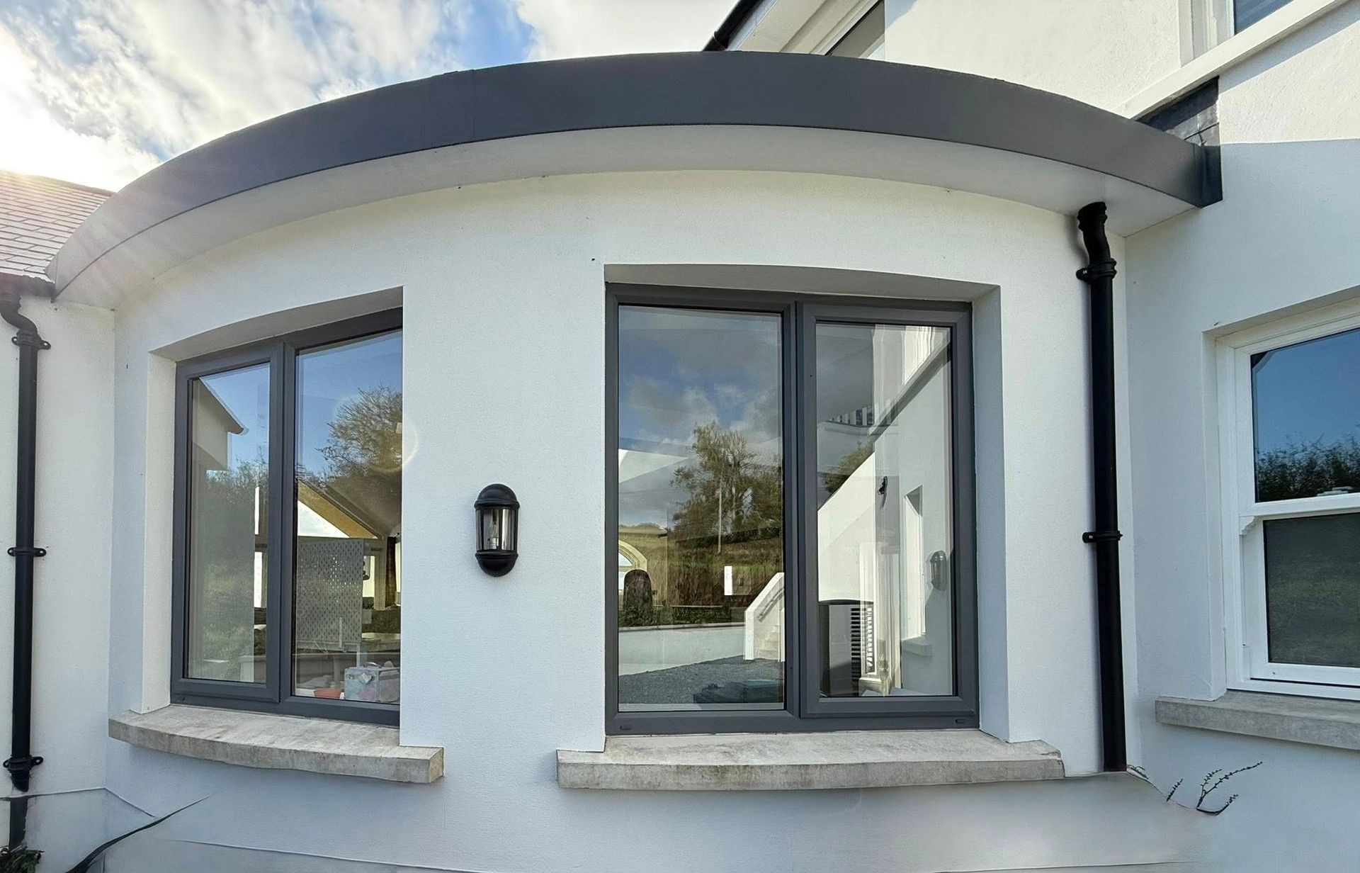 White building with curved roof, gray-framed windows, and stone sills.