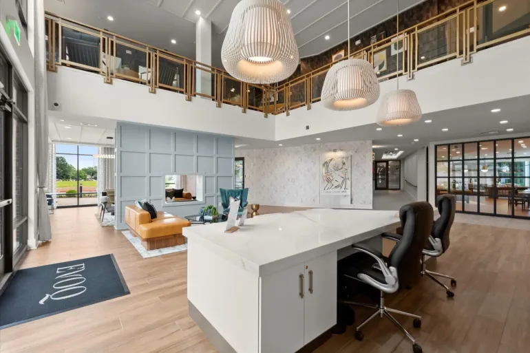 Bright modern lobby with white desk, high ceilings, large windows, and decorative hanging lights.