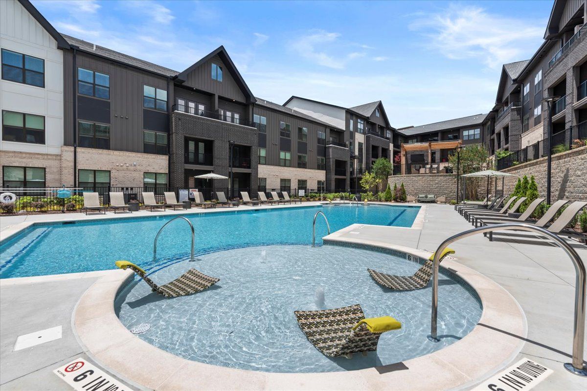 Apartment complex with tan siding, black shutters, and a walkway on a grassy lawn under a blue sky.