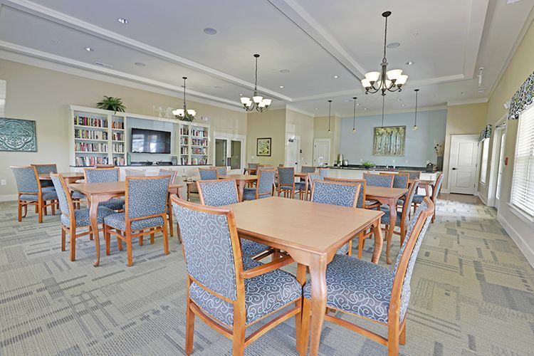 Empty community room with tables, chairs, bookshelves, and chandeliers.