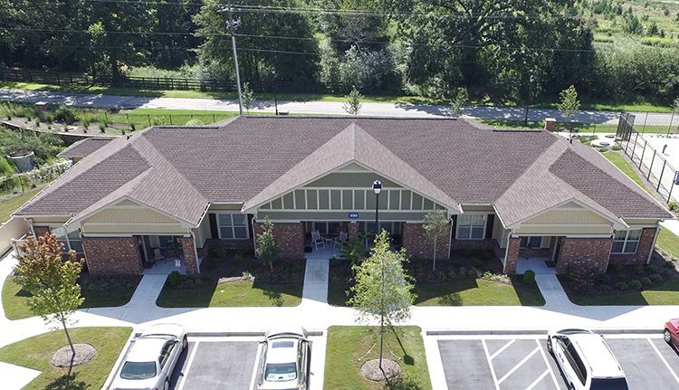Exterior view of a long, single-story building with a brown roof, red brick, and parking.
