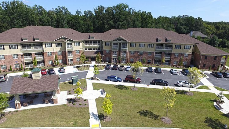 An aerial view of a three-story brick and beige building with a brown roof and a parking lot.
