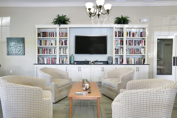Library seating area: four patterned armchairs face a bookcase with a TV and a small table.