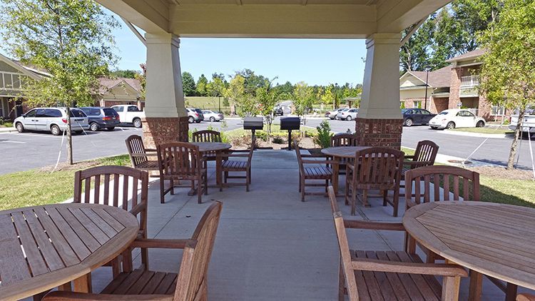 Outdoor pavilion with wooden tables and chairs, a grill, and cars parked nearby.
