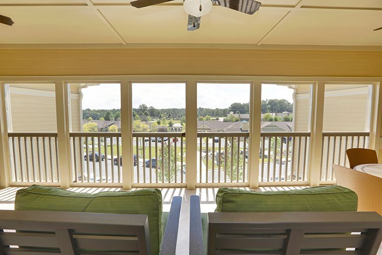 Two green cushioned outdoor chairs facing a wide, open view over a railing, from a covered porch.