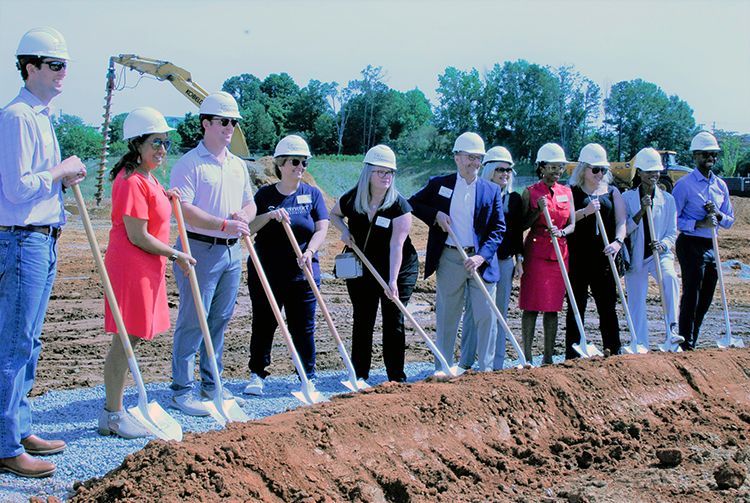 Group of people in hard hats and business attire holding shovels, ground-breaking ceremony.