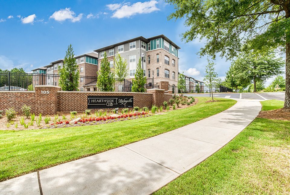 Apartment complex entrance sign with building in the background and a paved walkway.