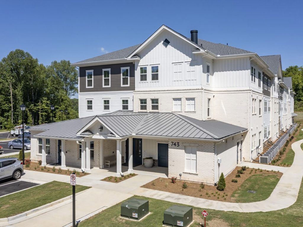 Multi-story apartment building with white and gray exterior, under a blue sky.