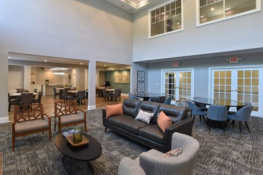 Spacious lobby with a dark leather sofa, patterned carpet, accent chairs, dining tables, and large windows.
