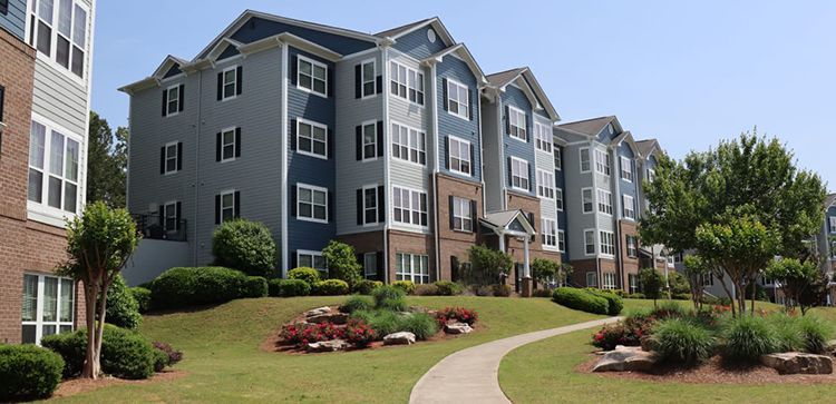 Apartment complex with a winding sidewalk through a grassy area, clear sky.