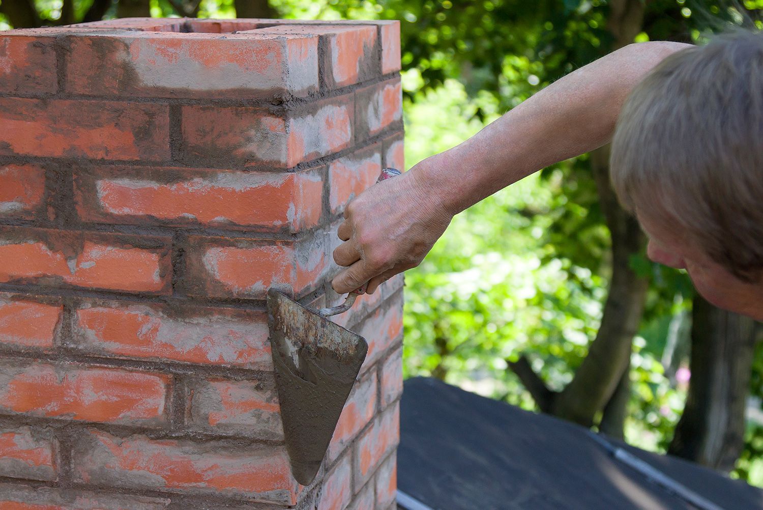 A man is applying mortar to a brick chimney.