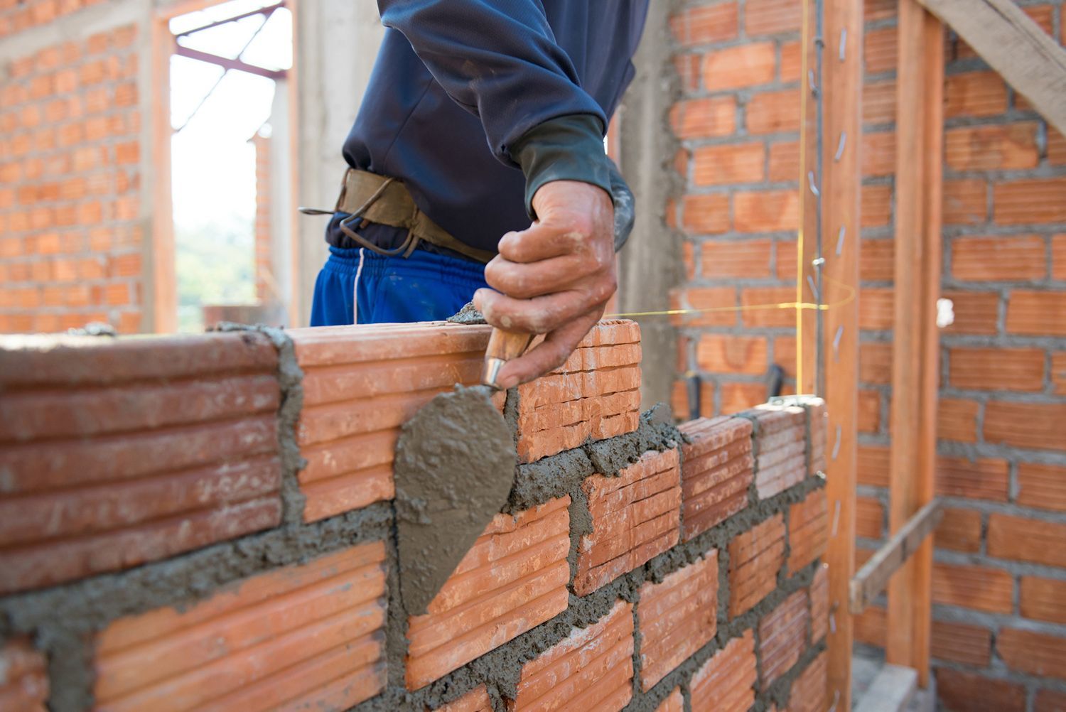 A man is laying bricks on a wall with a trowel.