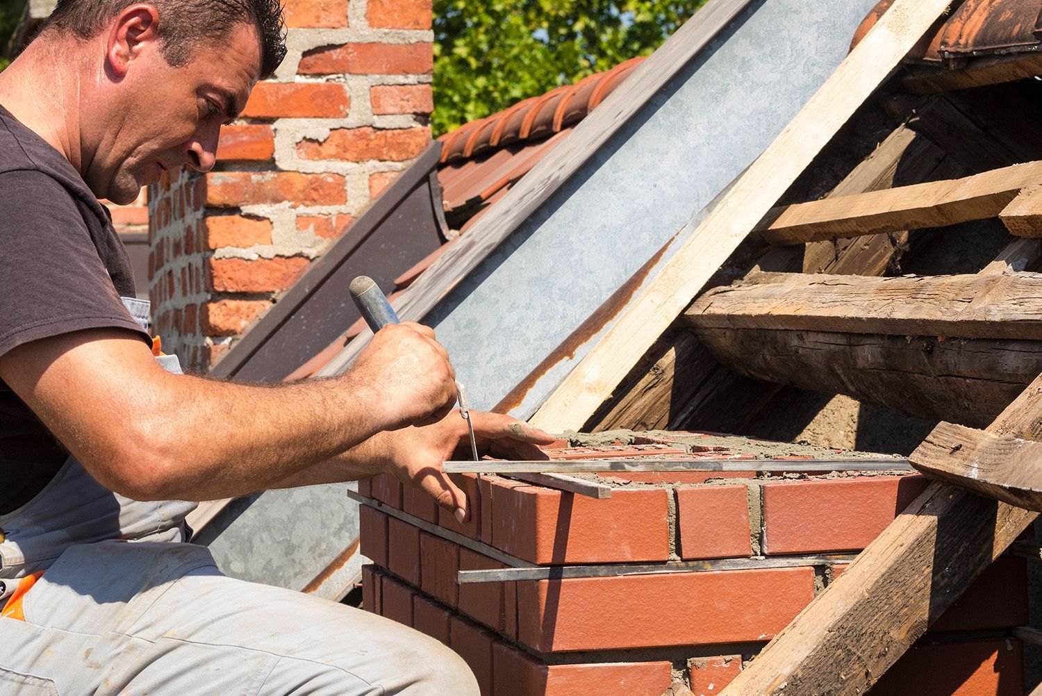 A man is working on a brick chimney on a roof.