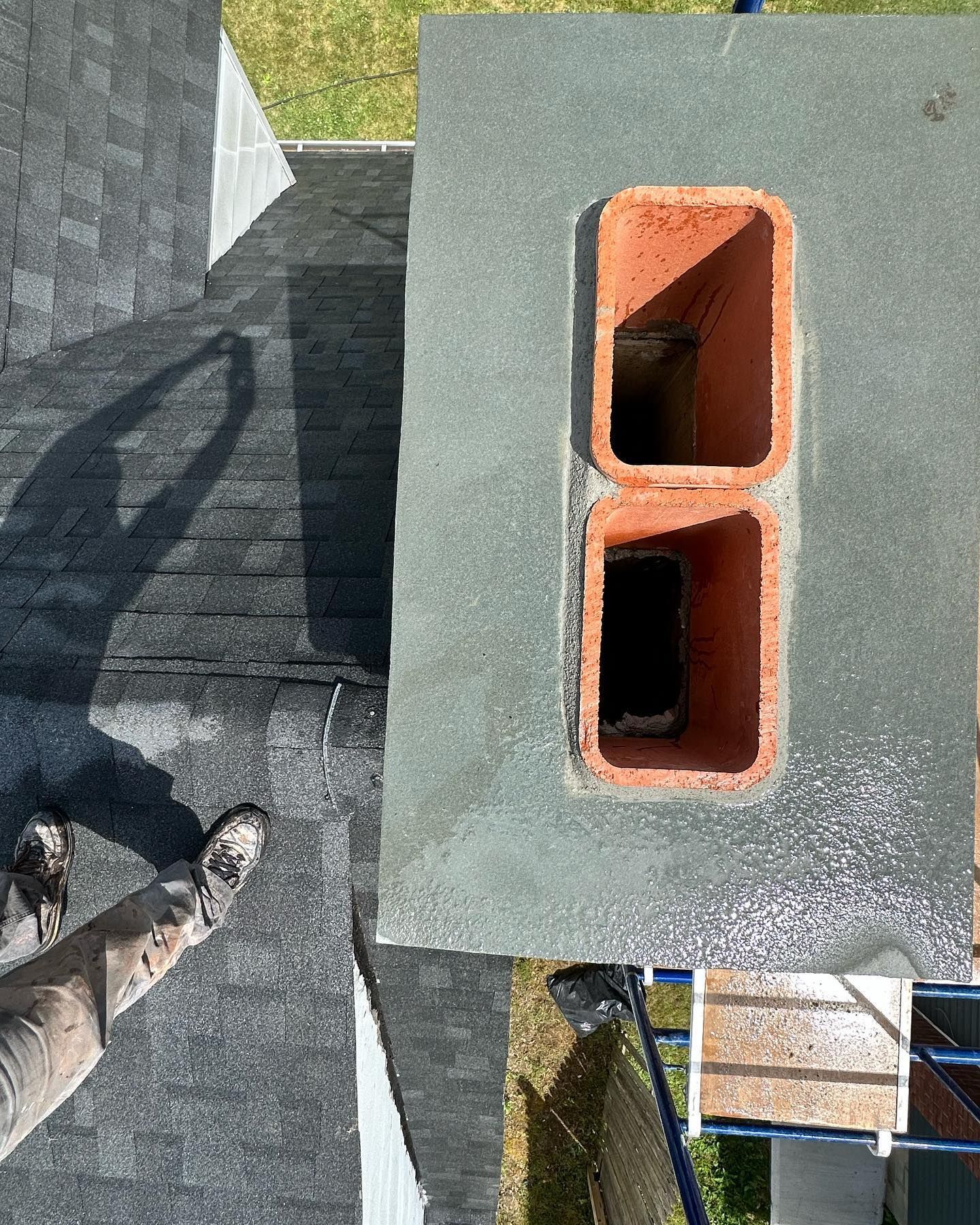 A man is standing on a roof next to a chimney.