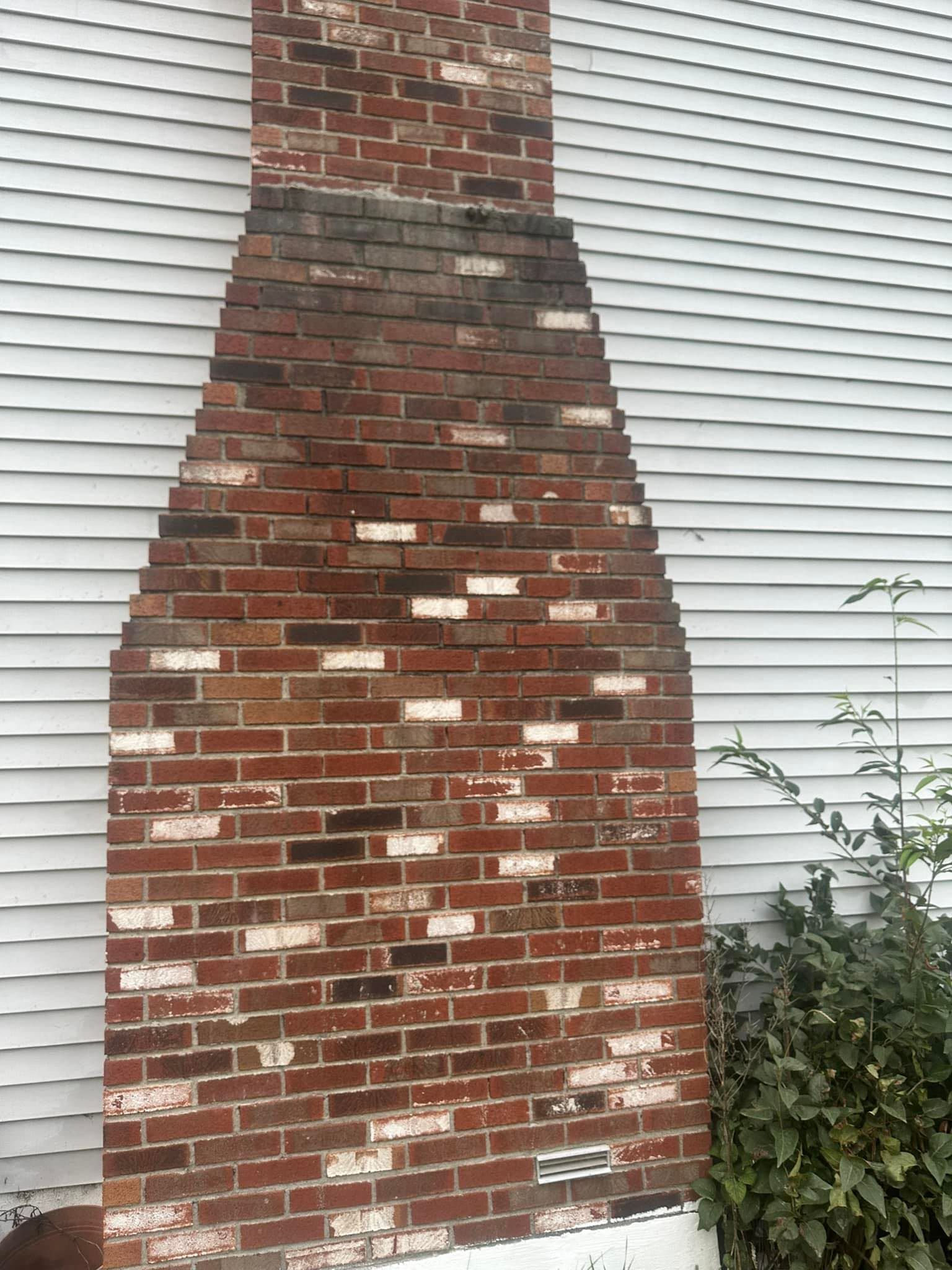 A brick chimney is sitting on the side of a white house.