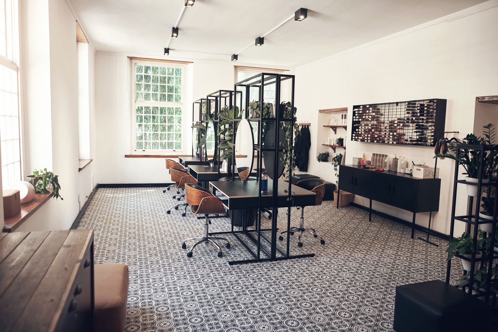 Bright office space with black desks, metal shelving, and plants. Large windows, patterned floor, and a black credenza.