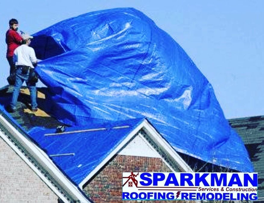 Two workers securing a large blue tarp over a residential roof, with the Sparkman Roofing & Remodeling logo below.
