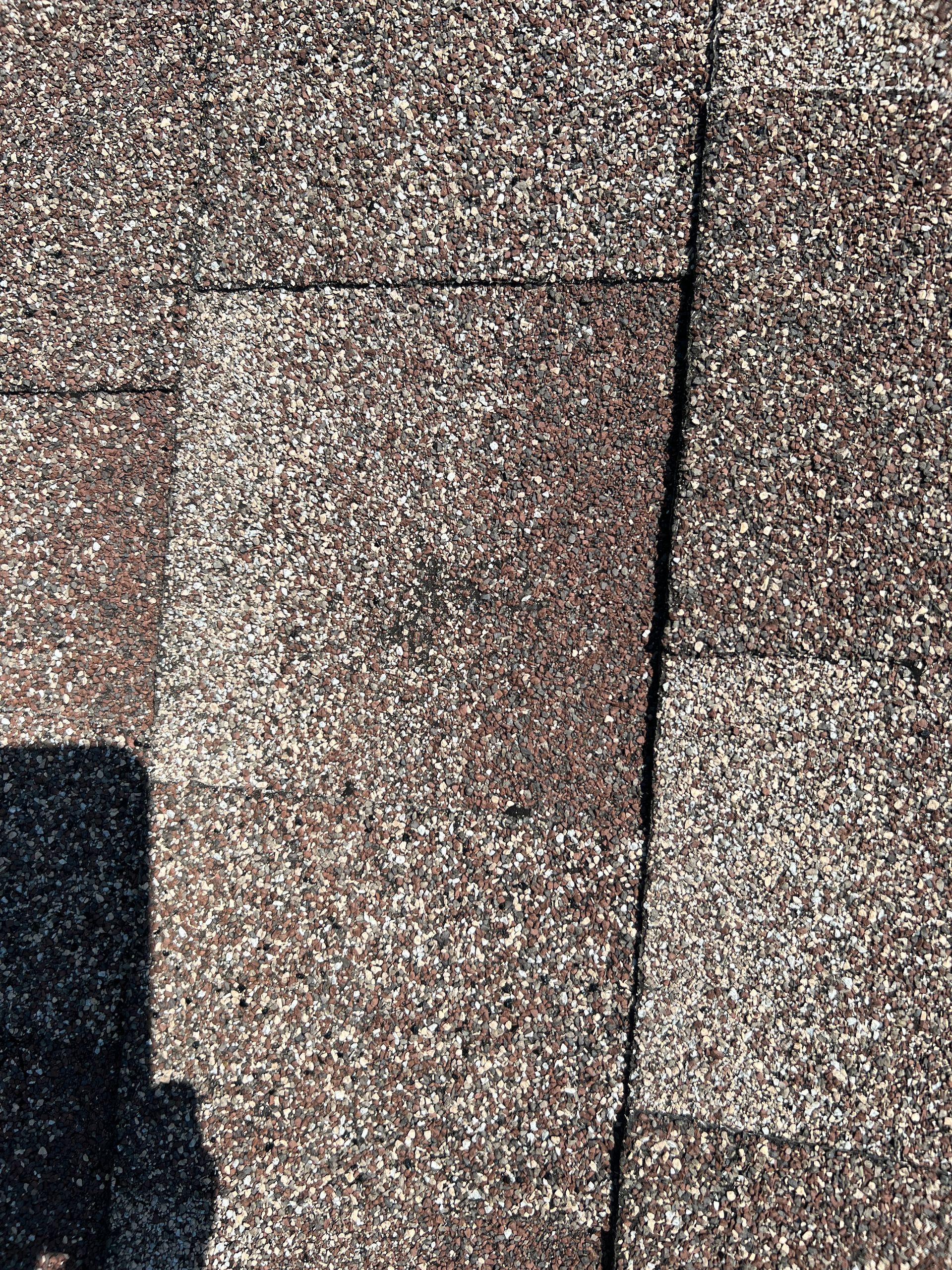Close-up of brown and tan architectural asphalt shingles on a roof showing a vertical seam between two shingles.